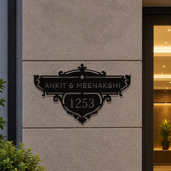 A custom black metal house number plaque mounted on a textured beige stone wall, featuring the names 'ANKIT & MEENAKSHI' and the number '1253' in elegant serif typography.