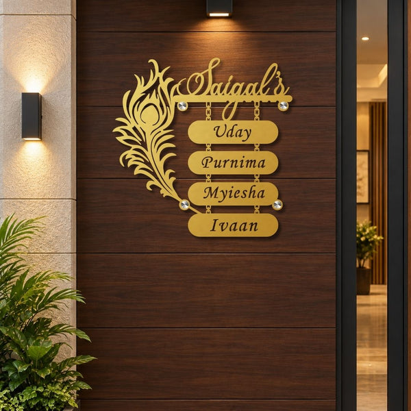 A personalized gold metal wall sign mounted on a dark brown wooden door. The sign features a decorative peacock feather on the left, the script name 'Saiyaal's' at the top, and four horizontal nameplates spelling 'Uday', 'Purnima', 'Myiesha', and 'Ivaan'.

