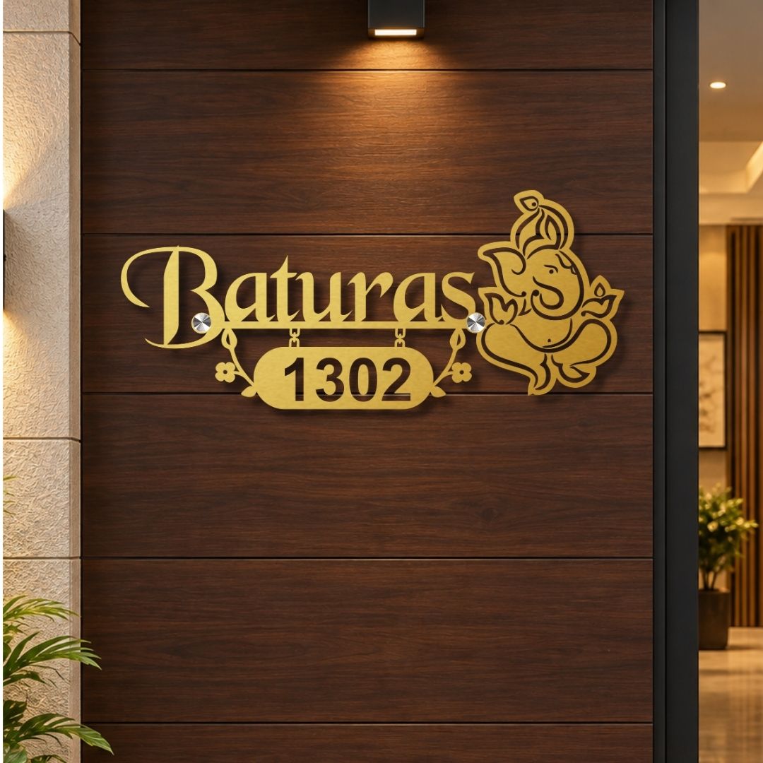Gold-colored custom house number sign featuring the name 'Baturas' in cursive, the number '1302' in a badge, and a Ganesha illustration, mounted on a dark wood-paneled exterior door.

