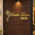 Custom gold metal house number sign with a traditional Ganesha emblem and the name 'Ravathi Mohan' on a dark brown wooden door.