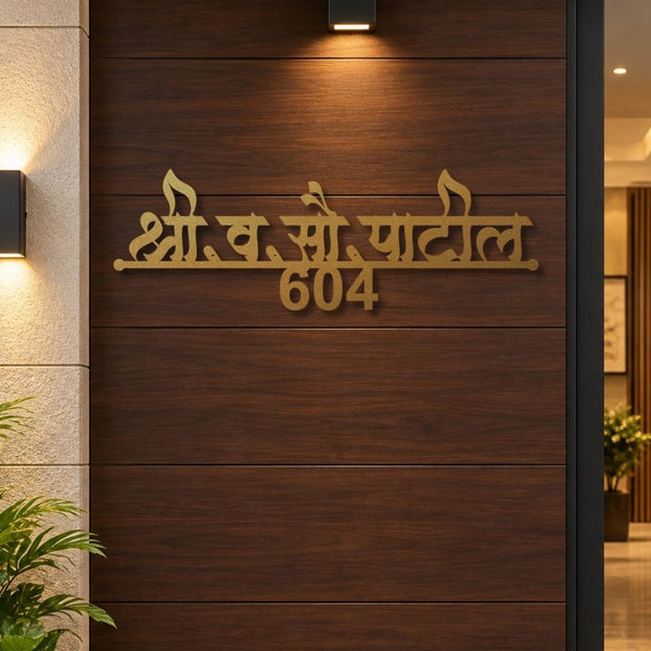 Gold-toned metal house number sign with Devanagari script and the number 604, mounted on a dark brown wood-paneled wall in an entrance setting.

