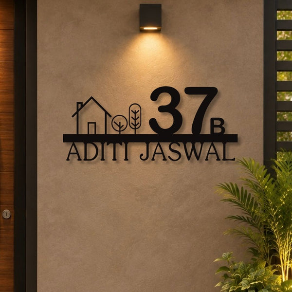 Custom black metal wall art featuring the number 37, a house outline, trees, and the name 'ADITI JASWAL' mounted on a beige stucco wall under a wall sconce.

