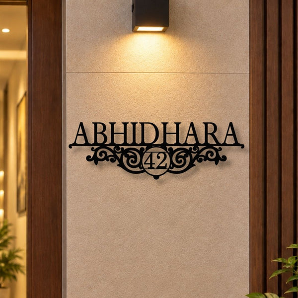 Black metal decorative wall sign reading 'ABHIDHARA 42' mounted on a beige textured wall, with a warm wall light above and wooden door frames on both sides.