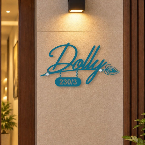 A teal metal custom wall sign featuring the script name 'Dolly' with a hanging number plate reading '230/3' and an arrow motif, mounted on a beige tiled wall under a black wall sconce.