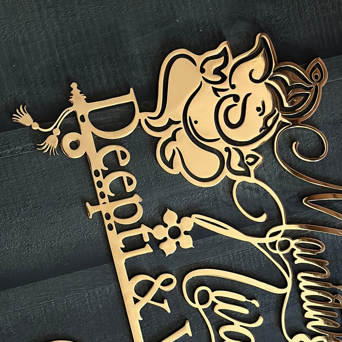 Gold-colored laser-cut metal sign featuring a silhouette of Radha Krishna, the script text 'Sweet Home Divya & Manish', and a hanging plaque with 'B-48', displayed against a dark textured wall.
