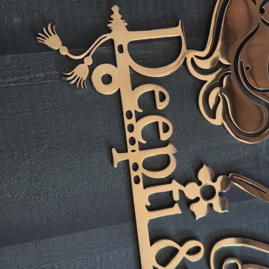 Gold-colored laser-cut metal sign featuring a silhouette of Radha Krishna, the script text 'Sweet Home Divya & Manish', and a hanging plaque with 'B-48', displayed against a dark textured wall.
