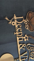 Gold-colored laser-cut metal sign featuring a silhouette of Radha Krishna, the script text 'Sweet Home Divya & Manish', and a hanging plaque with 'B-48', displayed against a dark textured wall.
